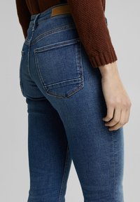 Tajta denimjeans i mörkblått, med hög midja, bakfickor och subtila sömnadsdetaljer, ihopsatta med en texturerad brun tröja.