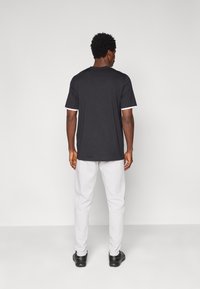 Μαύρο κοντομάνικο μπλουζάκι με λευκή λεπτομέρεια στο γιακά και στα μανίκια, συνδυασμένο με ανοιχτό γκρι παντελόνι και μαύρα παπούτσια.