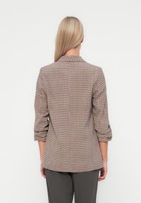 Brązowo-kremowa marynarka w kratę o dopasowanym kroju, z kołnierzykiem i rękawami do łokcia, wykonana z fakturowanej tkaniny.
