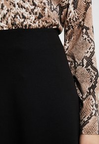 Černá látková sukně s hladkým povrchem, spárovaná s vzorovanou halenkou s hadím potiskem v hnědé a černé barvě, která má dlouhé rukávy.