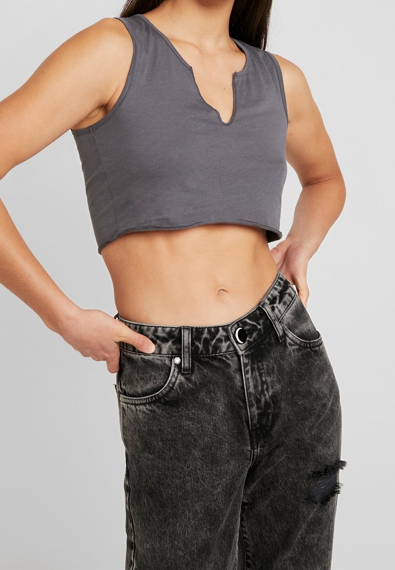 Top corto gris con escote en V, combinado con jeans de mezclilla negros desgastados con una cintura alta y textura desteñida.