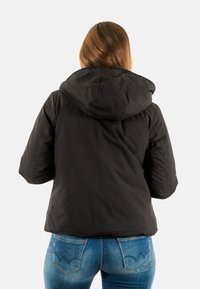 Giacca nera con cappuccio, dal design puffato e maniche larghe, realizzata in materiale morbido. Abbinata a jeans di denim blu.