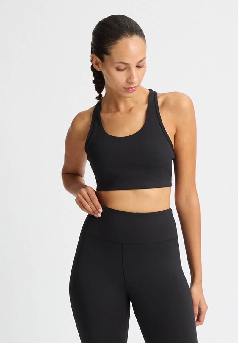 Czarny sportowy crop top z szerokimi ramiączkami i okrągłym dekoltem, w połączeniu z czarnymi legginsami z wysokim stanem, obie części charakteryzują się gładką fakturą.