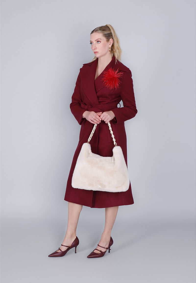 Bordeaux jas met een riem en rode bloemaccenten, met een crèmekleurige faux fur tas met een gevlochten schouderband, aangevuld met bordeauxpunten hiel.