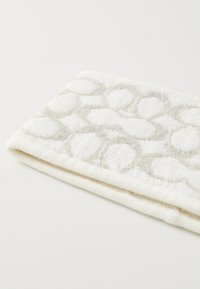 Λευκή πετσέτα με υφή που απεικονίζει επαναλαμβανόμενα οβάλ σχήματα σε ασημένιο νήμα, με απαλή και χνούδινη υφή. Διπλωμένη για παρουσίαση.