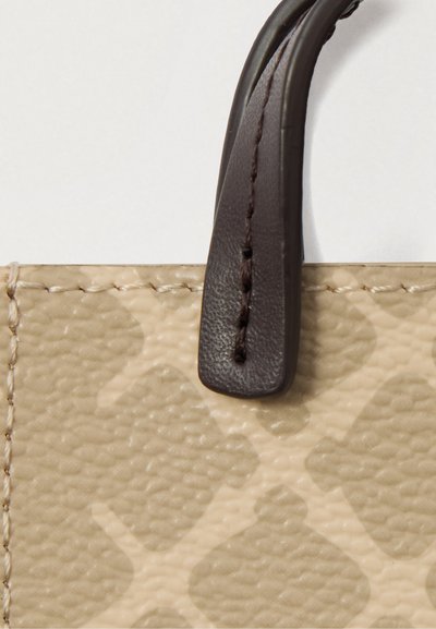 Beež tekstuurne kott nurgaosa, kus on hele muster ja tumepruun õmmeldud nahk käepide valgel taustal.