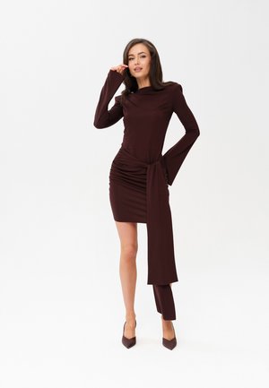 Długo-sleeve, burgundowa sukienka z elastycznego materiału, z marszczeniami z boku i asymetrycznym dołem. Dobierane do stroju wysokie szpilki dopełniają całość.