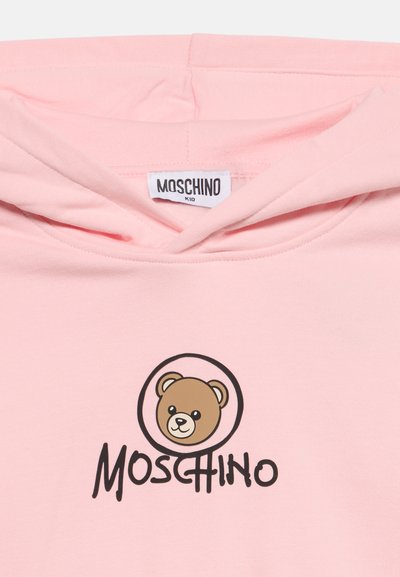 Sweat à capuche Moschino Kid rose clair avec un logo visage d'ours en peluche à l'intérieur d'un cercle et le nom de la marque Moschino en dessous en lettres noires.