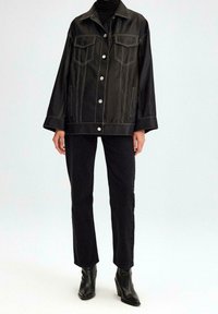 Zwarte leren jas met witte stiksels, oversized ontwerp, twee borstzakken en knoopsluitingen. Gecombineerd met zwarte rechte broek en enkelboots.