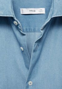 Lichtblauw denim overhemd met een klassieke kraag, knoopsluiting aan de voorkant met witte knopen en een textuurstof. Label zichtbaar bij de kraag.