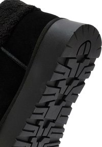 Czarny boot z teksturowanym wierzchem i gumową podeszwą, z wyraźnym wzorem bieżnika dla lepszego chwytu. Gładkie wykończenie wzdłuż krawędzi.