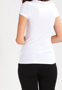 Bílá košile s krátkým rukávem, se slim fit střihem a hladkým, elastickým materiálem. Zobrazená zezadu, s zakřiveným lemem a bez viditelných log.