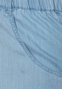 Tecido de denim azul claro com uma textura suave, apresentando uma cintura elástica e um detalhe de costura de bolso lateral.