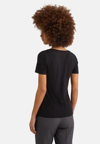T-shirt nero a maniche corte con scollo rotondo, materiale morbido e design aderente. La vista posteriore mostra una finitura pulita e cuciture sottili.
