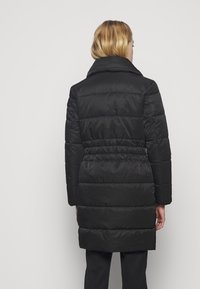 Abrigo acolchado negro con un cuello alto, cintura ajustada y mangas largas. Presenta secciones acolchadas y una tela suave y brillante.