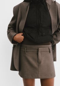 Brown textured short skirt with belt loops, paired with a black zip-up jacket featuring a hood and pockets. Both garments are tailored.