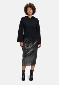 Felpa nera con cappuccio di paillettes, abbinata a una gonna plissettata argento lucido e stivali neri con tacco al ginocchio. Texture piatta.