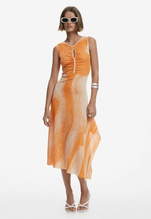 Vestido con estampado naranja y crema, con un corte en forma de ojal, cuerpo fruncido y dobladillo asimétrico. Llevado con gafas de sol blancas y calzado.