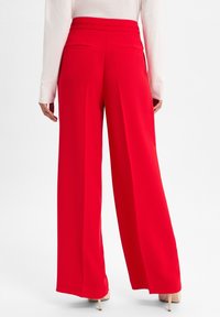 Rote weit geschnittene Hose aus glattem Stoff, mit hohem Taillenbund und zwei Gesäßtaschen, ergänzt durch ein langärmliges Oberteil.