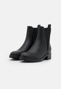 Bottes Chelsea en cuir noir avec panneaux latéraux élastiques, bout arrondi, finition texturée et un petit talon bloc avec un accent doré.