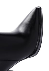 Vue latérale d'une chaussure à talon haut en cuir noir, avec un bout pointu et une texture lisse, offrant un éclat subtil et une semelle noire contrastante.