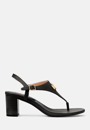 Sandale à talon en cuir noir avec un talon bloc, une bride de cheville avec boucle dorée et une bride avant style tanga avec détail décoratif doré.