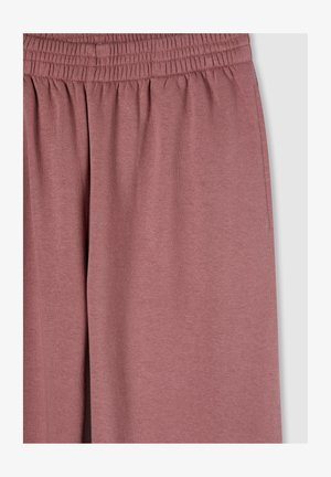 Pantaloni sportivi rosa morbidi e leggeri con vita elastica e dettagli di tasche laterali; il tessuto ha una consistenza liscia.