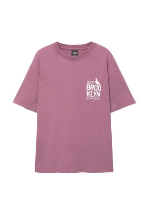 Lila pamut póló rövid ujjakkal, fehér "11202 BROOKLYN New York" felirattal és egy madár grafikával a bal mellrészén.