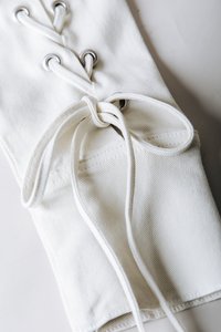 Λευκό ύφασμα με υφή διαθέτει οπές και κορδόνια. Ένας κόμπος στα κορδόνια είναι ορατός, παρουσιάζοντας ένα καθαρό, μινιμαλιστικό σχέδιο.