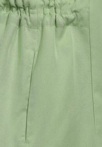 Jasnozielona tkanina o gładkim, lekko fakturowanym wykończeniu. Posiada marszczoną talię i boczną kieszeń. Prosty, czysty design.
