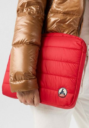Housse de portable rembourrée rouge avec un design matelassé, arborant un logo circulaire bleu et blanc. Tenue dans une main avec un manteau en duvet marron visible.