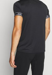 Svart atletisk t-shirt med korta ärmar, mjuk textur och kontrasterande vit logotyp på ärmen. Skräddarsydd passform, minimalistisk design.