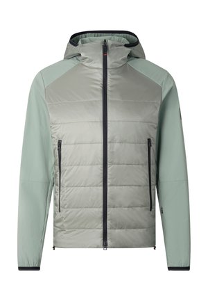 Young man wearing light green hooded jacket, matching pants, chunky sneakers, and large black sunglasses, standing with hands in pockets.