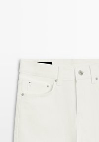 Weiße Jeans aus Denim mit flachem Bund, silberner Hardware und vorderen Taschen. Der Stoff wirkt glatt mit einer leichten Textur.