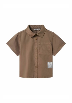 Chemise brune à manches courtes en coton, avec un col, une poche poitrine et une étiquette avec des détails textuels sur le bas.