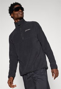 Pullover in pile nero con colletto alto, dotato di zip frontale, logo sul lato sinistro del petto e tessuto testurizzato. Vestibilità morbida e rilassata.