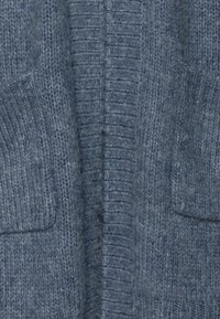 Neulottu neuletakki pehmeästä, sinisestä villasta, jossa on ribbineulos, pystysaumat ja kaksi etutaskua.