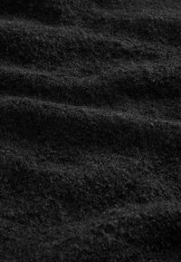Tissu en laine noire avec une surface douce et légèrement texturée, présentant des ondulations subtiles et de la profondeur dans le tissage du matériau.