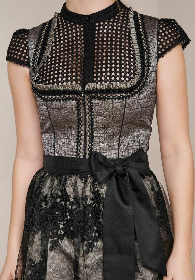 Schwarz-weißes Kleid mit einem strukturierten Oberteil mit Netzüberzug, Rüschensaum und einem Spitzenrock, der mit floralen Stickereien und einem Schleifen-Gürtel verziert ist.