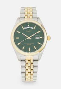 Montre-bracelet Timex avec un cadran vert, un bracelet en métal doré et argenté, affichage du jour indiquant vendredi, date affichant le 14, et marqueurs et aiguilles dorés.
