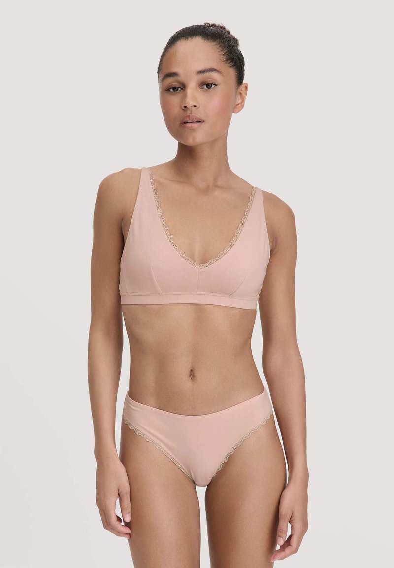 Lichtroze beha en bijpassende slip met kanten afwerking. De beha heeft een V-hals ontwerp en zachte stof, terwijl de slip een gladde afwerking heeft.