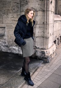 Giacca a vento nera, maglione nero, gonna grigia aderente con tasche, collant neri trasparenti e stivaletti neri alla caviglia con dettagli a coste.