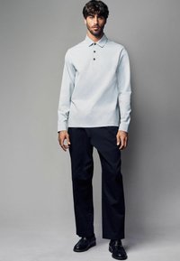 Polo de lungă mână de culoare gri deschis, cu guler și trei butoane, asociat cu pantaloni negri de costum și pantofi negri. Culori simple, uni.