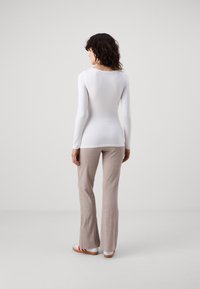 White long-sleeve top paired with light beige ribbed flared pants. Model wears white sneakers with red accents, seen from the back against a neutral backdrop.