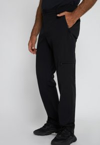 Zwarte outdoor broek van lichtgewicht stof, met ritszakken en een taps toelopende pasvorm, met een gladde textuur en een minimalistisch ontwerp.