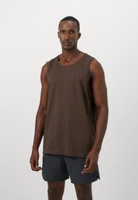 Brun tank top med rund halsudskæring og brede ærmegab, parret med mørkegrå shorts med et tekstureret mønster.