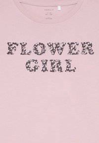 Lichtroze katoenen T-shirt met "FLOWER GIRL" in donkere bloemenpatroonletters. Rond de halslijn en korte mouwen.