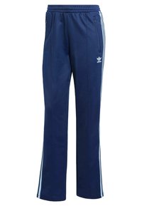 Tmavomodré teplákové nohavice Adidas s bielymi bočnými pruhmi, elastickým pásom, bočnými vreckami na zips a logom trefoil Adidas na stehne.
