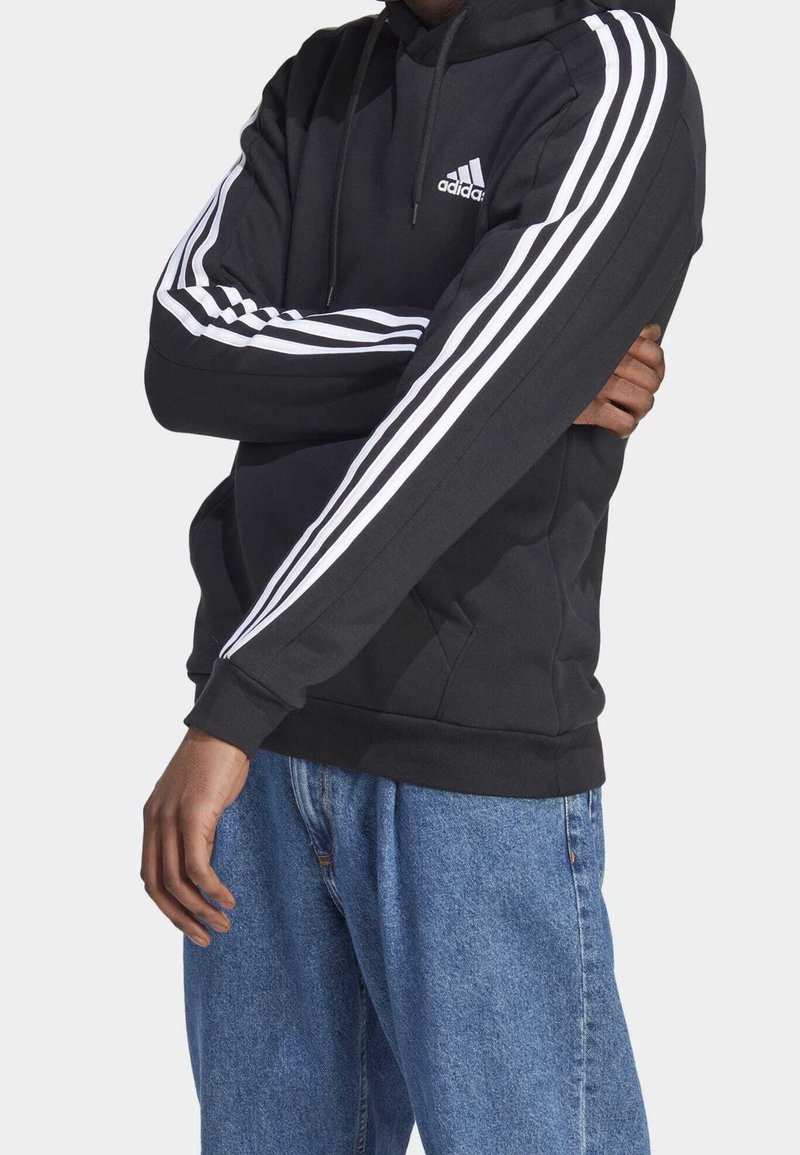 Sweat à capuche noir avec accents blancs à trois bandes sur les manches, doté d'une poche avant et d'un cordon de serrage ajustable pour la capuche.