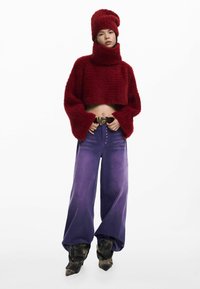 Pulover roșu, scurt, pufos, cu mâneci supradimensionate și pălărie asortată, combinat cu pantaloni largi mov și cizme cu vârf ascuțit, cu model.